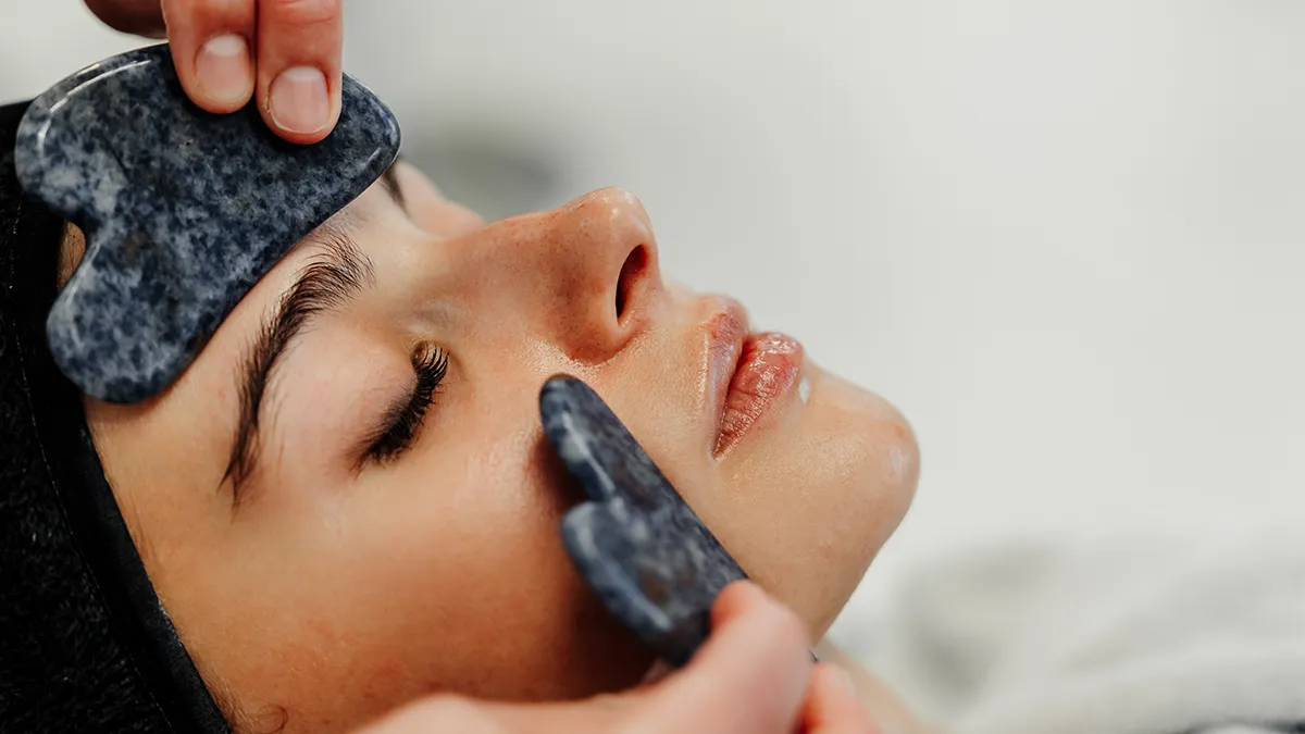 Woman getting a lymphatic drainage massage on the face with 2 gua sha tools